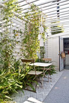 an outdoor patio with table and chairs surrounded by greenery on either side of the door