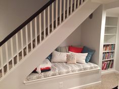 there is a small bed under the stairs in this room with bookshelves on either side