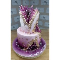 a three tiered cake with purple and gold decorations on it's side, sitting on a wooden table