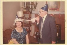 an older man and woman standing next to each other in front of a fire place