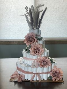 a three tiered wedding cake with pink flowers and feathers on the top, sitting on a table