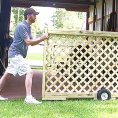 a man pushing a wooden crate on wheels in front of a shed with another man standing next to it