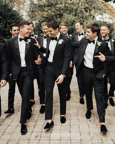 a group of men in tuxedos walking down a brick walkway together and smiling at the camera