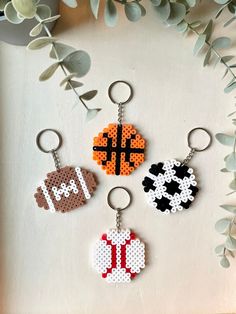 three key chains with different designs on them sitting next to some plants and flowers in front of a white background