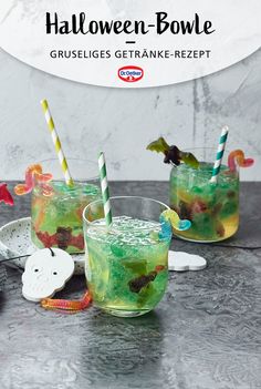 two glasses filled with green liquid and topped with halloween decorations, sitting on a table