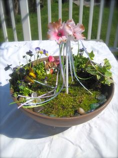 a bowl filled with plants and flowers on top of a white cloth covered tablecloth