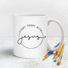 a white coffee mug with the words start today with jesus written on it next to colored pencils