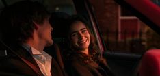 a man and woman sitting in the back seat of a car smiling at each other