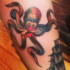 an octopus tattoo on the leg of a person with a boat in the water behind it