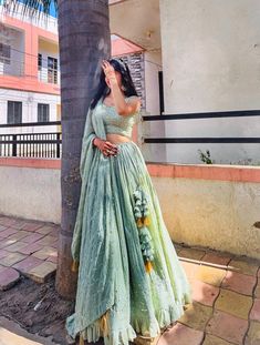 a woman standing next to a palm tree wearing a green and yellow dress with flowers on it