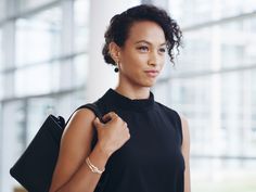 a woman in a black dress is holding a handbag and looking at the camera