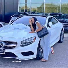 a woman leaning on the hood of a white mercedes benz car in front of a dealership