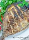 grilled fish on a white plate with green garnish and red hot peppers