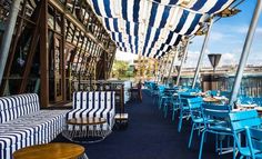 an outdoor dining area with blue and white striped chairs, tables and umbrellas over looking the water