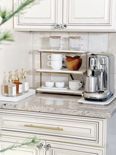 a kitchen with white cabinets and marble counter tops is pictured in this image, there are dishes on the shelves