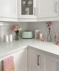 a kitchen with white cabinets and pink flowers in vases on the counter top next to a toaster oven