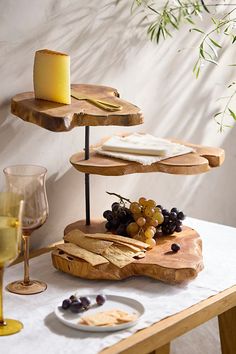 three tiered tray with cheese, crackers and grapes next to wine glasses on a table