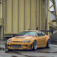 an orange sports car parked in front of a large metal structure on a rainy day