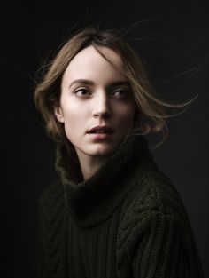 a woman in a green sweater with her hair blowing in the wind, looking directly into the camera