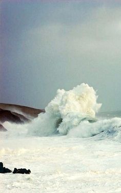 a person standing on top of a snow covered slope next to the ocean and crashing waves