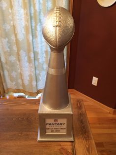 a silver trophy sitting on top of a wooden table in front of a curtained window