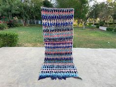 a multicolored knitted blanket sitting on top of a cement slab in the middle of a park