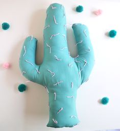 a blue cactus pillow sitting on top of a white table next to green pom poms