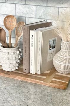 some books and wooden spoons are on a shelf next to a potted plant