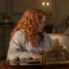 a woman with red hair sitting at a table in front of a golden box on it