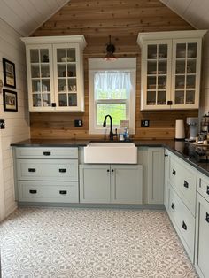 a kitchen with white cabinets and black counter tops in an attic style home that has wood paneling on the walls