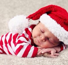 a baby wearing a santa hat sleeping on the floor with its eyes closed and hands under his chin