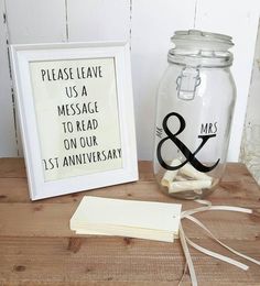 a glass jar with a wedding message in it on a table next to a sign that says, please leave a message to read on our 1st anniversary