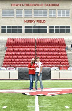 two people standing on the field in front of an empty bleachers with their arms around each other