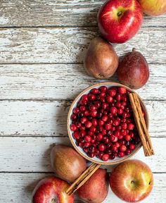 apples, cinnamon sticks and cranberries in a bowl on a white wooden table