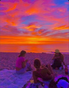 three people sitting on the beach at sunset with their backs to each other and one person holding a cell phone