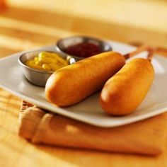 two hotdogs on a plate with mustard and ketchup in small bowls