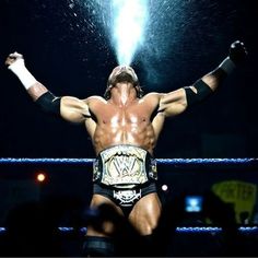 a man standing on top of a wrestling ring holding his hands up in the air