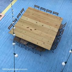 an overhead view of a wooden table and chairs on a blue deck with string lights