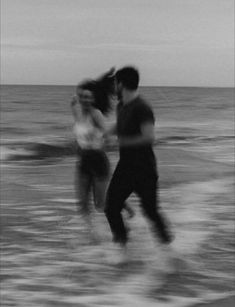 black and white photograph of two people walking on the beach with waves crashing in front of them