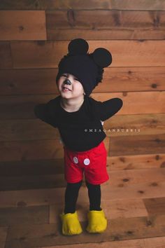 a young child wearing mickey mouse ears and red shorts, standing in front of a wooden wall