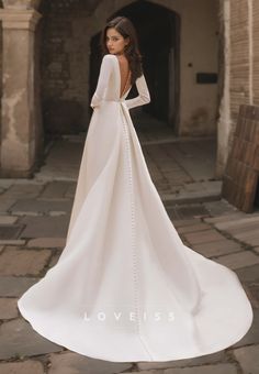 a woman in a white wedding dress standing on a stone walkway with her back to the camera