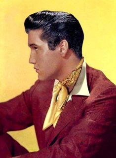 a man in a red suit and yellow tie sitting at a table with his hands on his knees