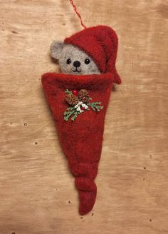 a teddy bear in a red christmas stocking hanging on a wooden wall with pine cones