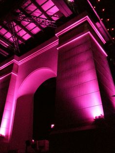 purple lights shine on the side of a tall building with columns and arches at night