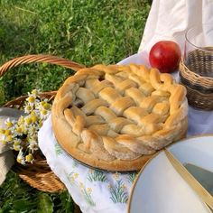 an apple pie sitting on top of a white table cloth next to a basket filled with apples