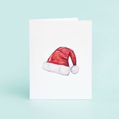 a card with a red santa hat on it's front and bottom corner, against a light blue background