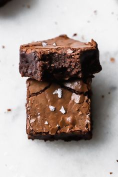 two pieces of chocolate brownie sitting on top of a white counter next to each other