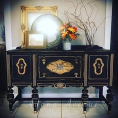 an ornate black and gold painted dresser with flowers on the top, in front of a mirror