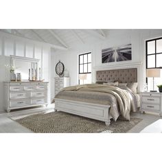 a bedroom with white furniture and windows in the background, including a bed, dresser, mirror, and chest of drawers