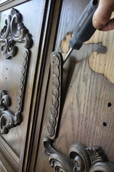 a person using a screwdriver to fix an ornate door handle on a wooden cabinet